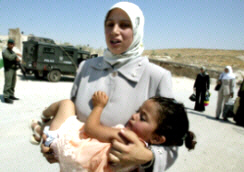 Beit Sahour 116, August 4, 2003, Photo above: A Suffring at an Israeli checkpoint, Photo by:  Nayef Hashlamoun.  A Palestinian mother caries her daughter in a sunny hot day as tries to pass an Israeli checkpoint of Wadi al-Nar near of the West Bank city of Beit Sahour. Israeli army blocked the roads around the Palestinian cities south of Jerusalem for Palestinian control.
